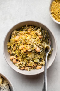 spinach and artichoke casserole topped with vegan parmesan in grey bowl on stone background