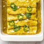 spinach and mushroom enchiladas with salsa verde in white baking dish topped with fresh jalapeno and cilantro