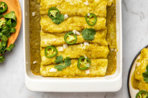 spinach and mushroom enchiladas with salsa verde in white baking dish topped with fresh jalapeno and cilantro