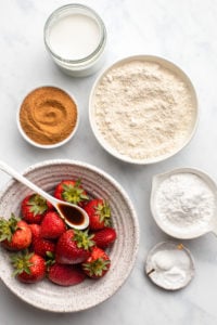ingredients for strawberry upside down cake in white bowls on marble background