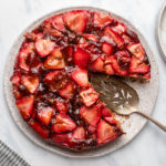 Vegan strawberry upside down cake with slice cut out on white serving platter on marble background
