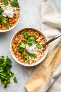 two bowls of vegan white bean chili topped with jalapeno, cilantro, and vegan cheese