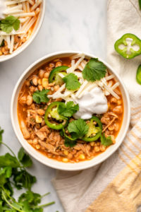bowl of vegan white bean chili topped with jalapeno, vegan cheese, and vegan sour cream