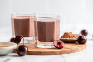two glasses of chocolate cherry almond smoothie with fresh cherries, cacao powder, and almond butter