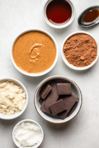 ingredients for chocolate almond butter bars in small white bowls on stone background