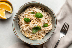bowl of vegan lemon ricotta pasta topped with fresh basil with lemon wedges and fork on side