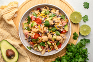 bowl of vegan taco pasta salad on wood serving tray with avocado, cilantro, and lime