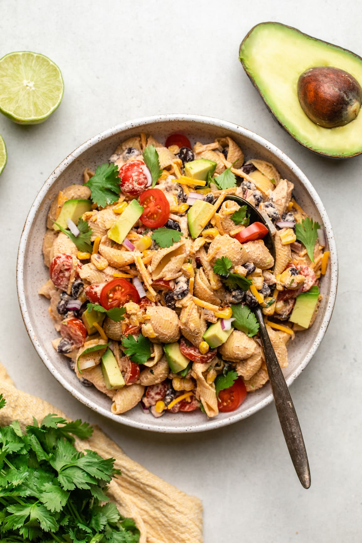 bowl of vegan taco pasta salad with serving spoon and avocado and cilantro on the side