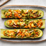 3 stuffed zucchini boats on white plate on marble background