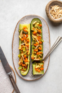 two stuffed zucchini boats on white plate with fork and side dish of slivered almonds