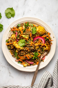 curried lentil salad topped with fresh cilantro on white plate with spoon and striped napkin