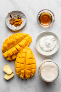 ingredients for golden milk mango smoothie organized on marble background