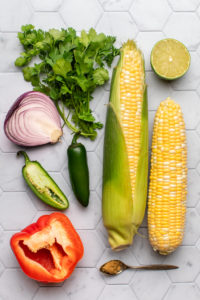 raw ingredients for pan grilled corn salsa on tile background