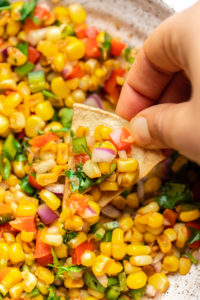 hand dunking tortilla chip into bowl of pan grilled corn salsa