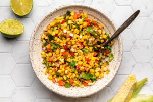 bowl of pan grilled corn salsa on tile background with limes on the side