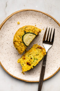 savory zucchini muffin cut in half on white plate with fork