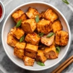bowl of sweet chili tofu topped with green onions with sweet chili sauce on the side