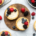mini berry tarts arranged on wooden serving tray topped with fresh berries
