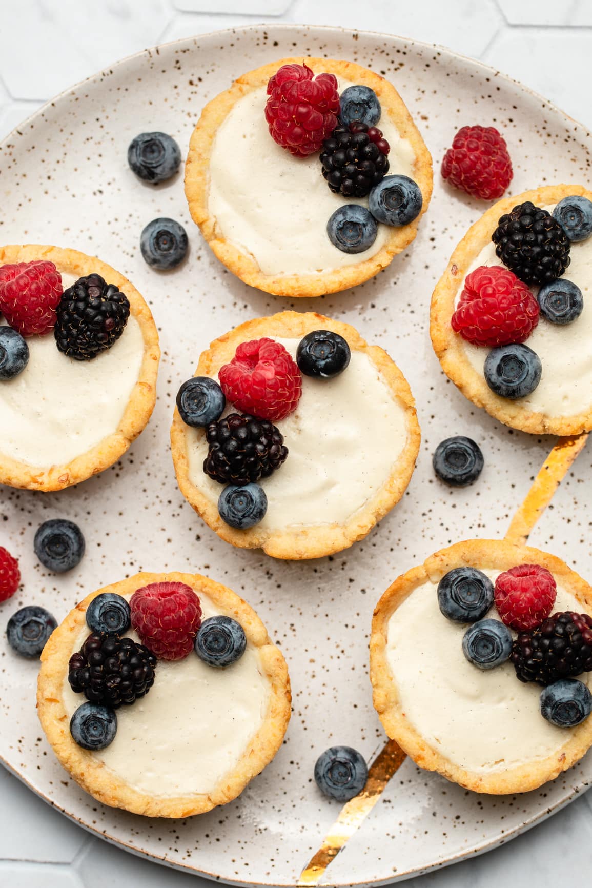 vegan berry tarts topped with fresh berries on white speckled plate
