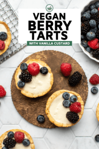 two berry tarts on wood serving board topped with fresh berries