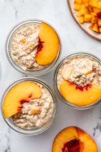overhead photo of 3 jars filled with peaches & cream overnight oatmeal and topped with a peach slice