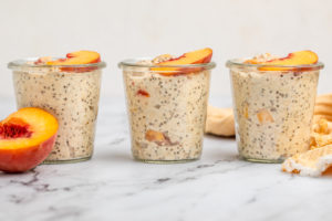 3 jars of peaches and cream overnight oatmeal topped with fresh peaches on marble table