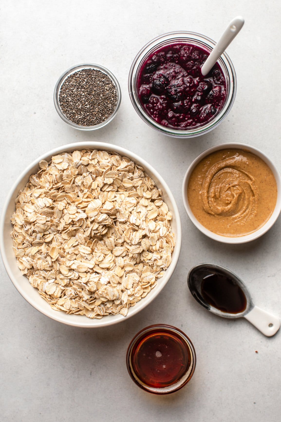 ingredients for pbj oatmeal bars in white bowls on marble background
