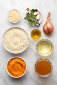 ingredients for pumpkin risotto in small white bowls on marble background