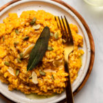 plate of pumpkin risotto garnished with oil, fried sage, and pumpkin seeds