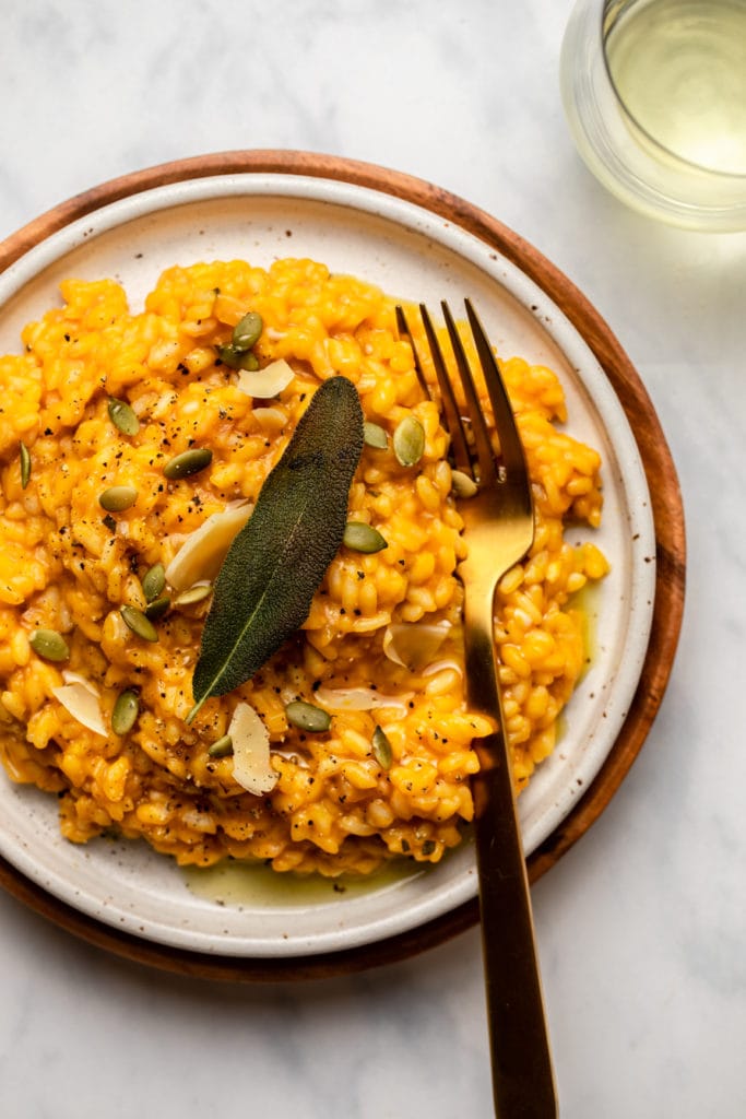 plate of pumpkin risotto garnished with oil, fried sage, and pumpkin seeds