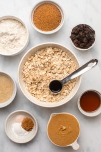 ingredients for cinnamon raisin oatmeal cookies in small white bowls on marble backgrounds
