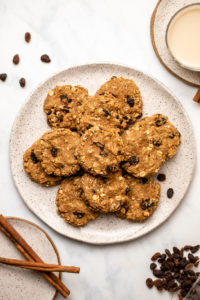 plate of cinnamon raisin oatmeal cookies on marble background next to cinnamon sticks and glass of milk