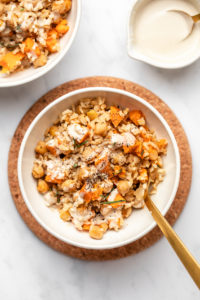 sweet potato rosemary casserole in white serving bowl topped with tahini dressing and black pepper