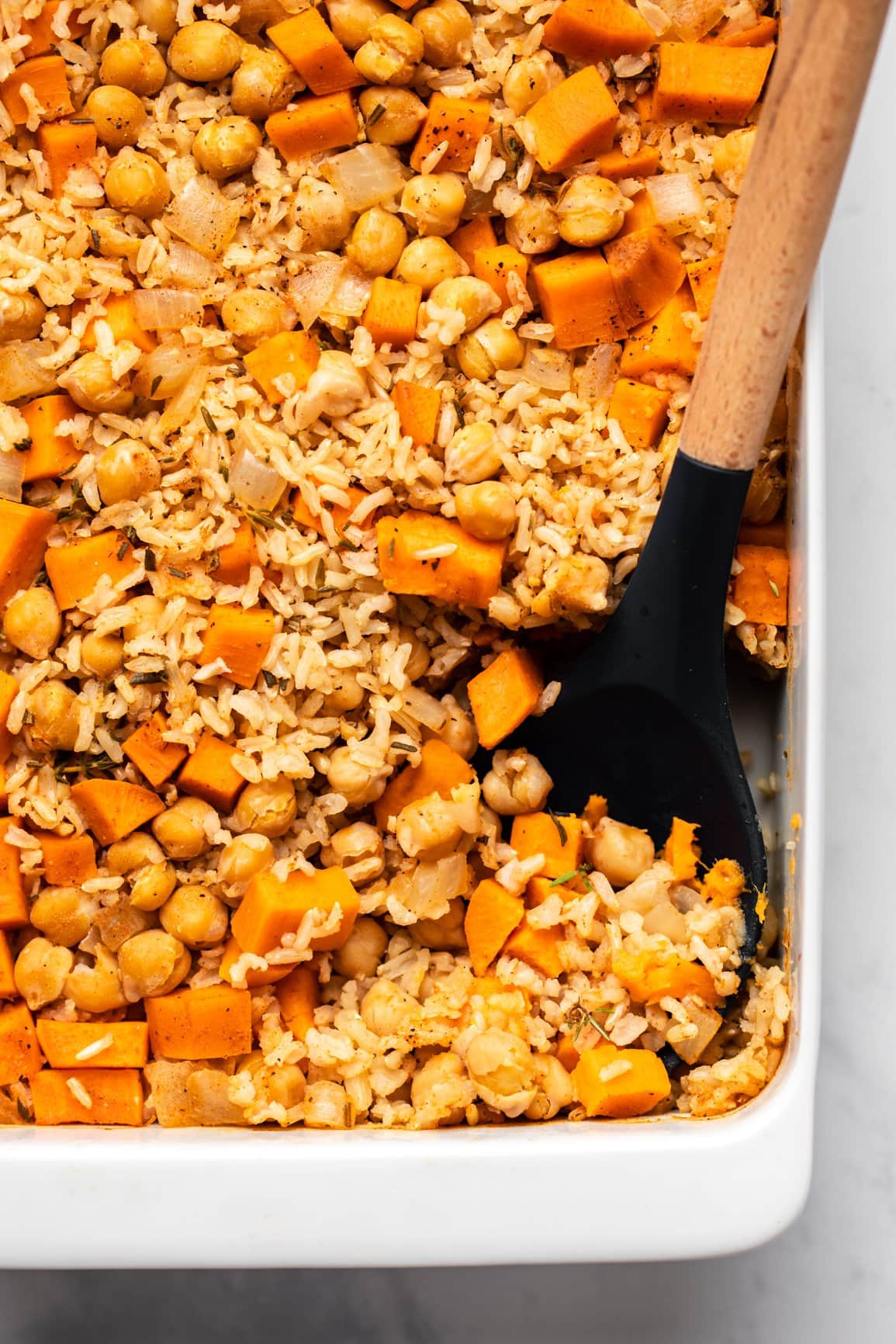 rosemary sweet potato casserole in white pan with wooden spoon scooping out casserole