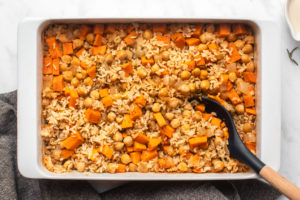 Dump and bake sweet potato rosemary casserole in white baking dish with wooden serving spoon on marble background