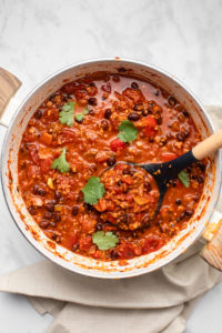 big pot of chorizo chili garnished with cilantro and with serving spoon