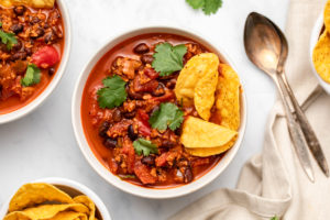 two bowls of vegan chorizo chili topped with cilantro and served with tortilla chips on the side