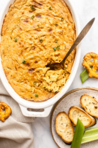 baked vegan crab dip in white dish served with bread, celery, and pretzel crackers