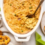 baked vegan crab dip in white serving dish with pretzel chips, bread, and celery sticks