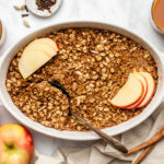 large white baking dish of apple chai baked oatmeal topped with fresh apples