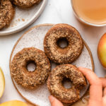 hand reaching for apple cider donut on plate with glass of apple cider and fresh apple on the side