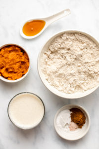 ingredients for fluffy pumpkin pancakes in white bowls on marble background