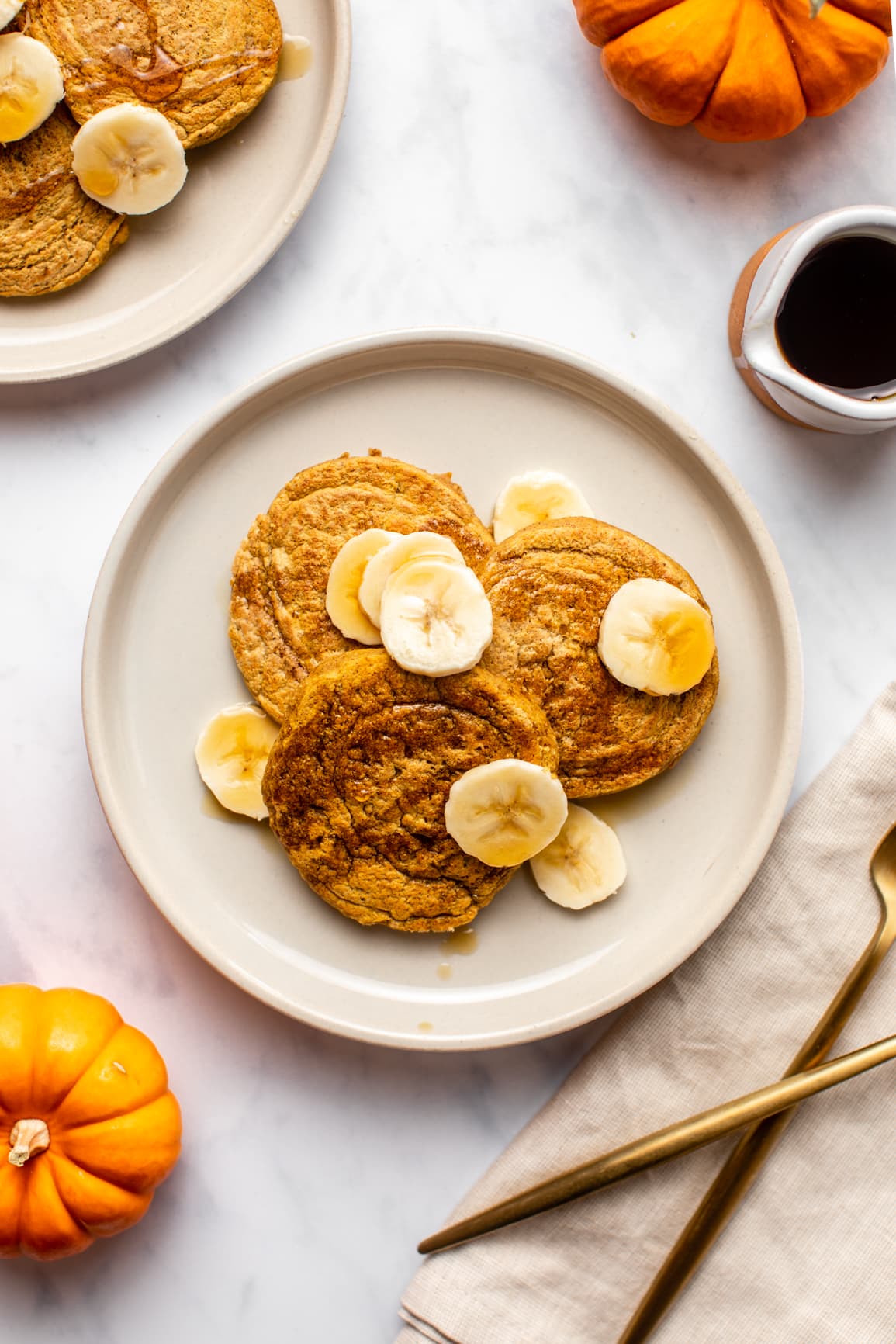 two plates of pumpkin pancakes topped with banana and maple syrup on marble background