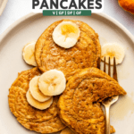 3 pumpkin pancakes on white plate topped with banana and maple syrup with fork bite taken out of one of them