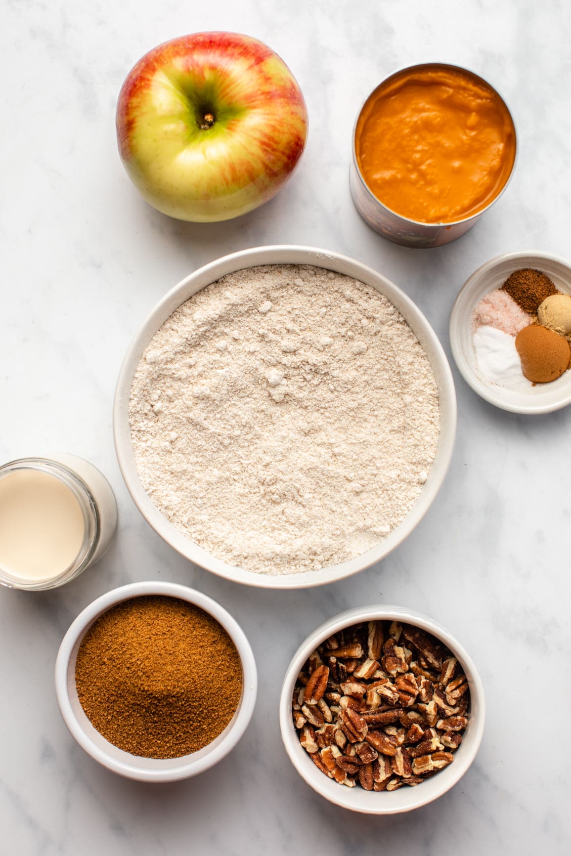 ingredients for pumpkin apple muffins in small white bowls on marble background