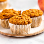 3 pumpkin apple muffins on white plate with small pumpkin and apple in the background