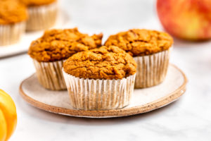 3 pumpkin apple muffins on white plate with small pumpkin and apple in the background