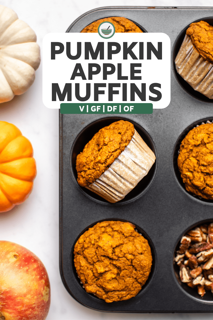 muffin tray filled with baked pumpkin apple muffins next to two small pumpkins and an apple