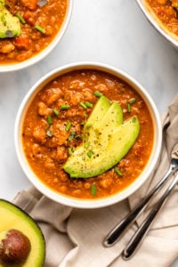 bowl of pumpkin chili topped with avocado, fresh thyme, and chives