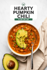 bowl of pumpkin chili topped with avocado, thyme, and chives with spoon and half an avocado on the side